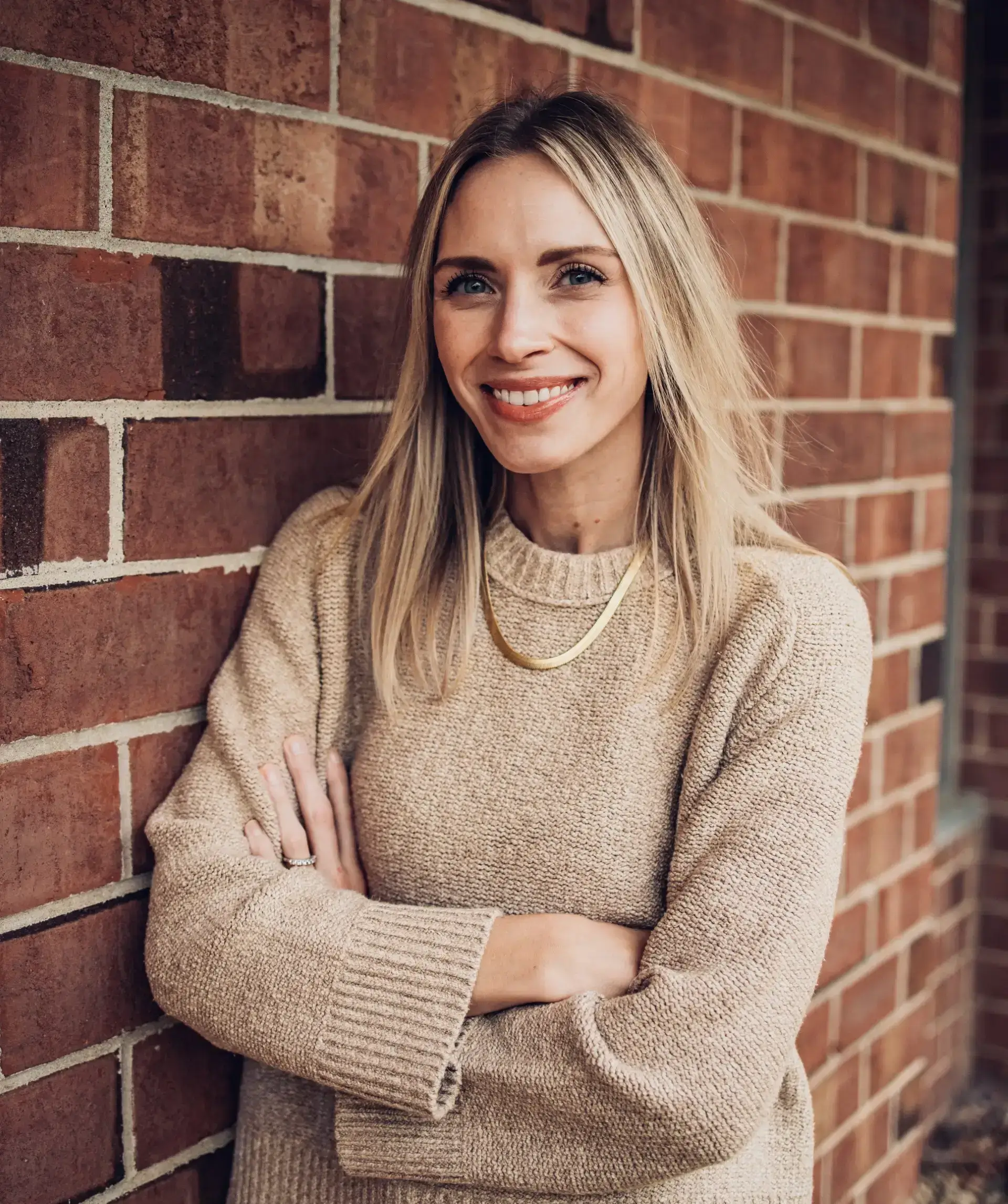 Smiling woman leaning against brick wall.